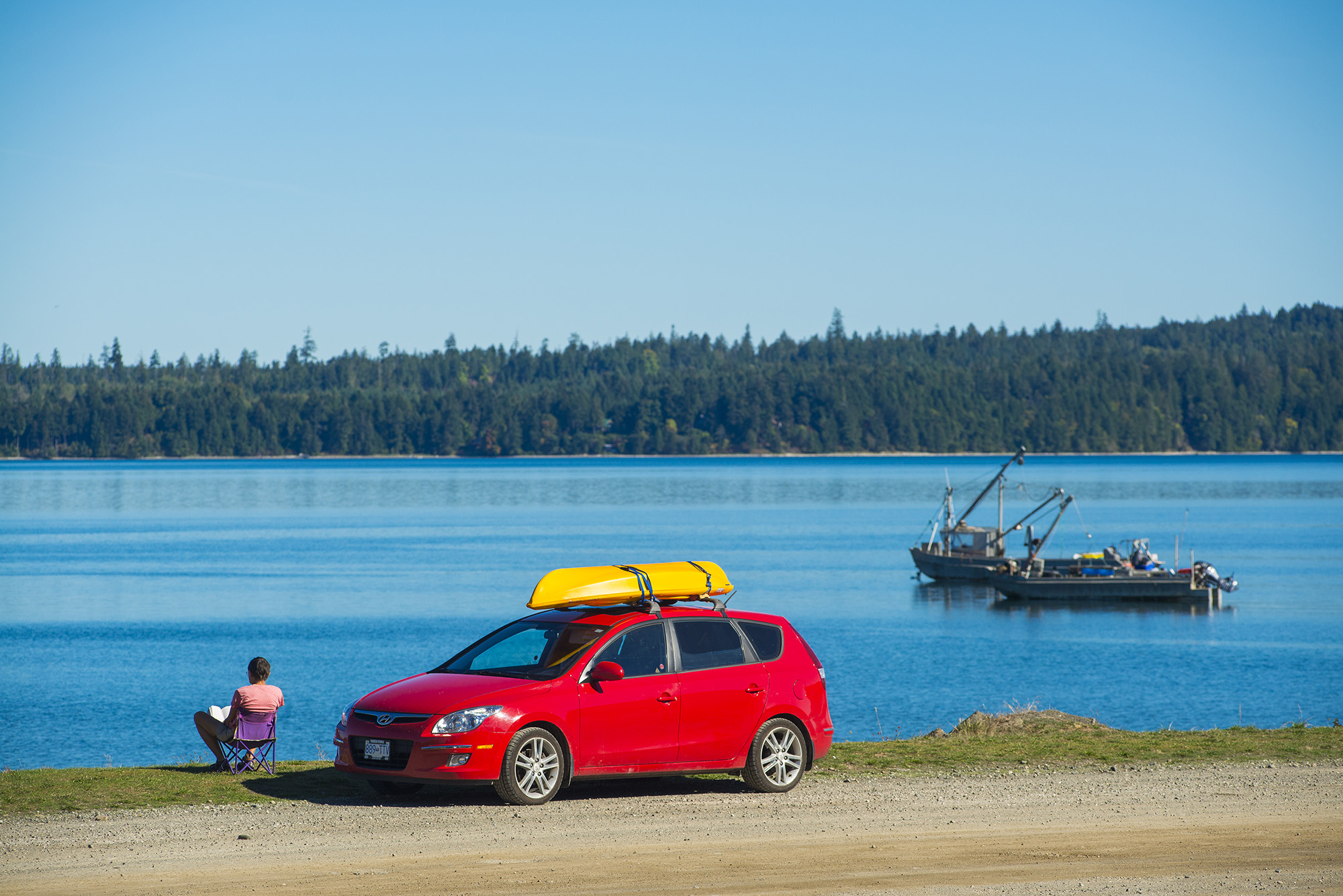 Frau mit Kanu auf dem Auto sitzt am Meer und liest, Royston, Strait of Georgia, Insel Vancouver Island, British Columbia, Kanada